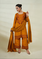 Woman wearing a mustard yellow traditional outfit with embroidery on a beige background