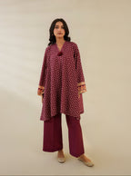 Woman wearing a maroon patterned outfit with gold accents on a beige background