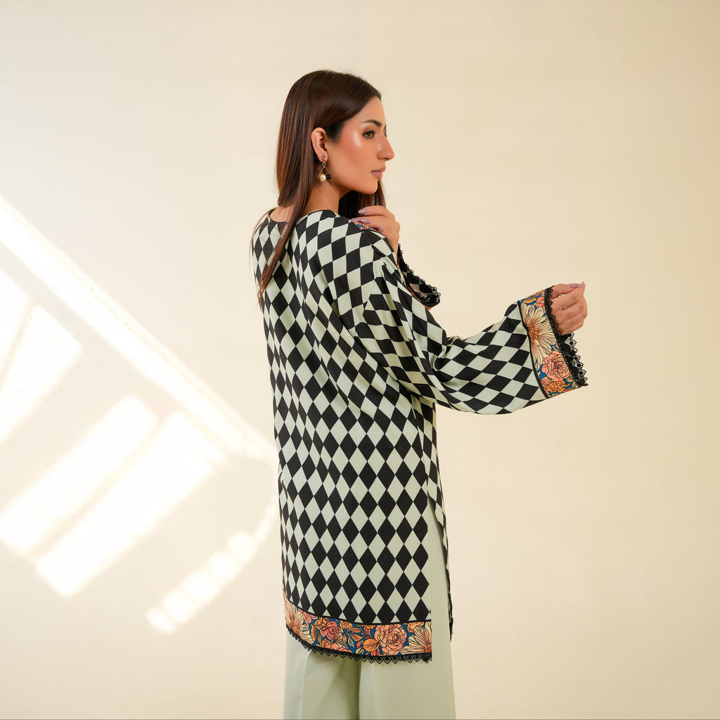 Woman wearing a black and white checkered dress with floral patterns on sleeves and hem against a neutral background